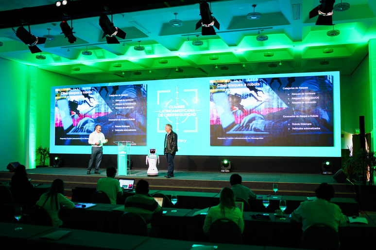 Robot Eva en el escenario de un congreso, entre dos expositores y ante el público