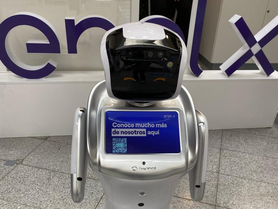 Robot Eva ante las letras corpóreas de una marca, mostrando un código QR en su pantalla táctil