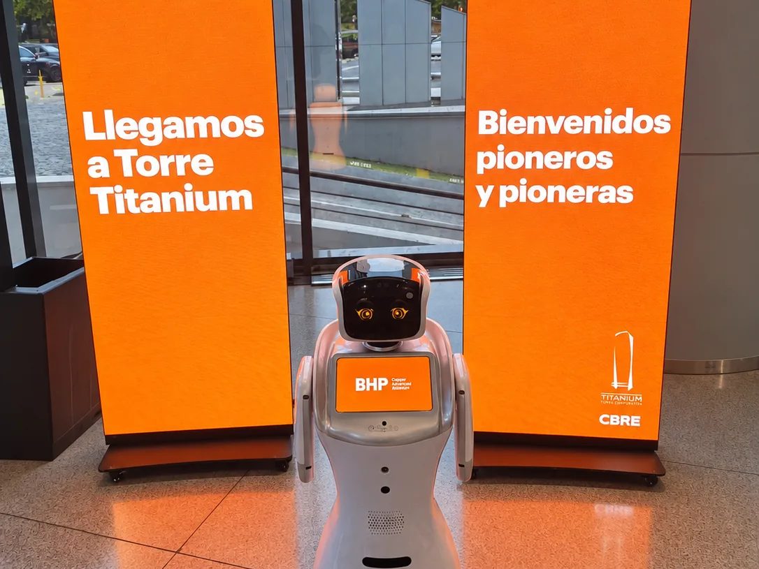 Robot Eva recibiendo a los invitados en el vestíbulo de un edificio corporativo, entre dos pendones de bienvenida