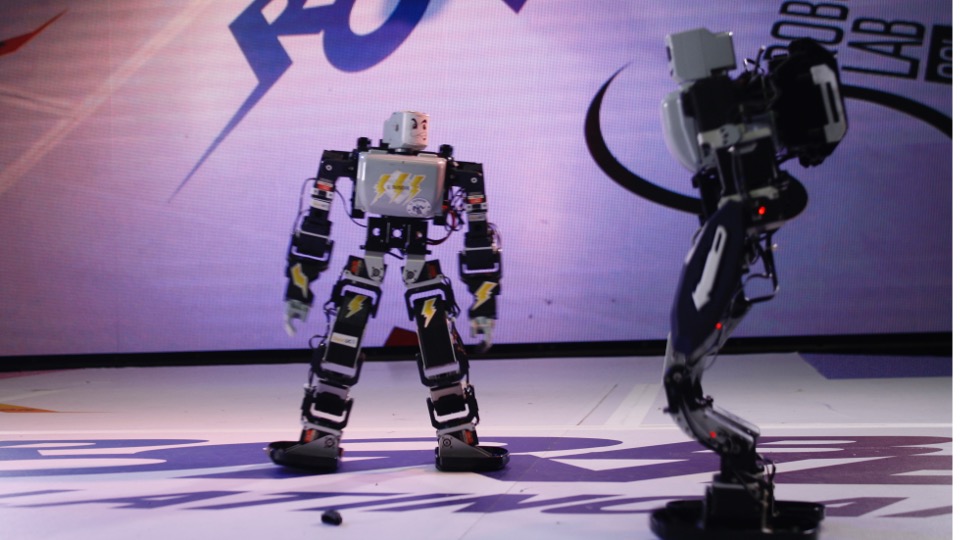 Dos robots bípedos enfrentándose sobre un escenario iluminado